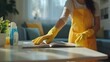 © orendesain99 - A woman in a yellow apron is cleaning a table with a yellow sponge