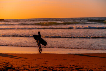 Wall Mural - A man is walking on the beach with a surfboard