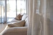 © Anna - Comfortable Beige Sofa with Cushions Behind Sheer White Curtains in a Sunlit Room