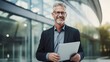 © CStock - A confident middle-aged businessman wearing a dark suit standing in front of a modern glass office