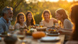 © Anastasiia Havelia - A heartwarming family gathering, with multiple generations gathered around the table for dinner in an outdoor setting, sharing laughter and stories under the warm sunset light.