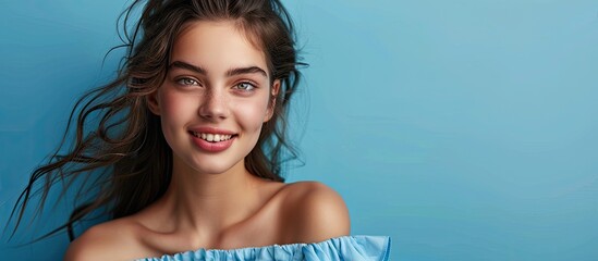 Poster - A young brunette female model in blue summer attire poses with a wide smile in front of a blue background offering room for copy space image