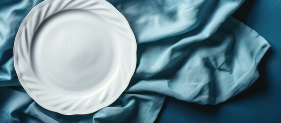 Poster - White porcelain plate on linen covering a blue background ideal for food styling with ample copy space image