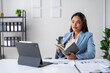 © Wasana - A woman is sitting at a desk with a laptop and a notebook