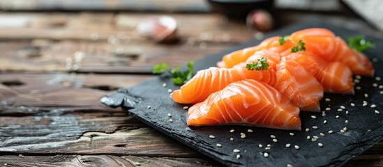 Sticker - A display of fresh salmon sashimi on a black stone plate atop a wooden table featuring a background with sufficient copy space for Japanese cuisine