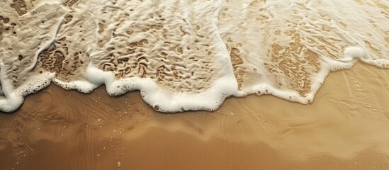 Fototapete - Soft waves gently caress the sandy beach creating a natural abstract background with copy space image