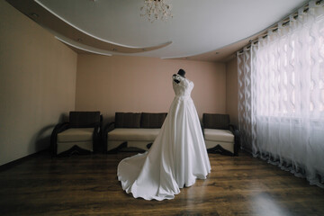 A woman in a white dress stands in a room with a couch and a chair. The room is empty and the woman is the only person in it