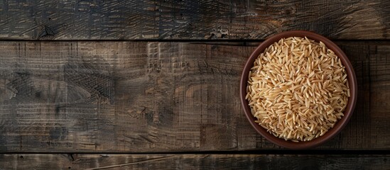 Poster - Top view of uncooked long grain brown rice in a bowl on a wooden surface with space for additional images