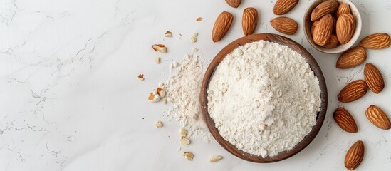 Poster - Top view of almond flour in a bowl and nuts on a white marble table with copy space image available