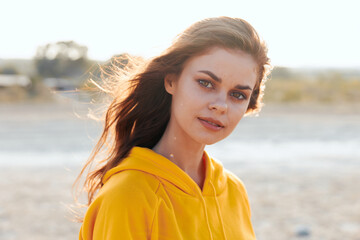 Wall Mural - Woman in yellow hoodie enjoying a breezy day at the beach with hair blowing in the wind