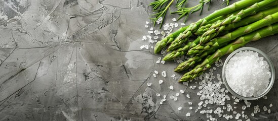 Poster - Top view of fresh green asparagus next to sea salt on a textured grey table with ample space for text in the image