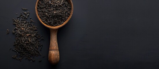 Poster - Close up of black tea leaves in a wooden spoon on a dark background with copy space image