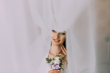 A woman is wearing a veil and holding a bouquet of flowers. She is smiling and looking at the camera