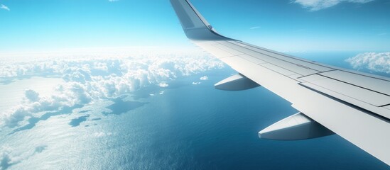 Poster - Wing of an airplane above the ocean with a blue sky and clouds. with copy space image. Place for adding text or design
