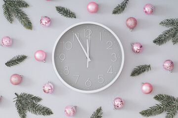 Creative trendy Christmas pattern made with pink Xmas baubles, green snowy Christmas tree branches and gray and white wall clock on gray background. Minimal Christmas eve or New Year idea. Flat lay.