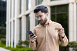 © Liubomir - Young man feeling stressed while holding smartphone and credit card in urban setting. Financial concern and frustration evident as he checks digital transaction.