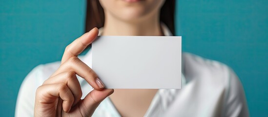 Leinwandbilder - A woman s hand is holding a blank white business card against a blue background serving as a mockup. with copy space image. Place for adding text or design