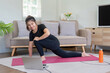 © Natee Meepian - Smiling Woman Practicing Virtual Yoga in Cozy Living Room