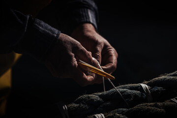 The hands of a fisherman repairing fishing nets with needle and thread.