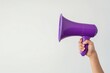 © srenhouse - Hand holding a purple megaphone on a white background