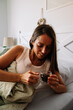 © AlbertoRodriguez - A woman is laying in bed with a cup of coffee in her hand. She is smiling and she is enjoying her drink