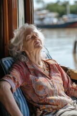 Wall Mural - A woman is sitting on a chair by a window, looking out at the water. She is relaxed and content