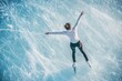 © Artsaba Family - An aerial view of a figure skater with arms outstretched, gliding across a blue ice surface leaving trails of ice shavings behind