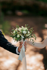 Wall Mural - A couple holding hands and a bouquet of white flowers. The man is wearing a suit and the woman is wearing a white dress. Scene is romantic and intimate