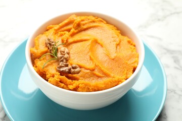 Delicious mashed sweet potatoes with walnuts in bowl on white marble table, closeup