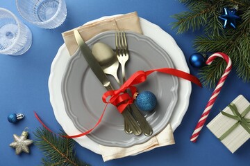 Beautiful Christmas setting with plates, elegant cutlery and festive decor on blue table, flat lay