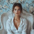 © Margarita - A beautiful girl in a white shirt sits on a white chair in a beauty salon against a background of dark blue wallpaper with white flowers. Retro image in bohemian style. A model poses