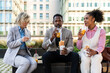 © oneinchpunch - Group of multiethnic business people meeting outdoors during lunch pause from work - International corporate business team bonding in the city and eating take-away salad and sanwiches