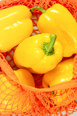 Wall Mural - Yellow bell peppers in orange mesh bag, emphasizing vibrancy of seasonal vegetables and their role in sustainable, mindful diet. Concept of healthy food and eco-friendly living. Vertical format