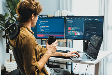 Working IT developer holding coffee cup with looking online software on pc at modern office on coding application screens, creating updated latest program firmware information version concept. Gusher.