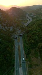 Wall Mural - Vertical aerial view of highway in the mountains between dense forest at sunset. Tunnel in the mountains. Movement