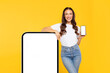 © Home-stock - Lady leaning on big cellphone with blank screen, showing smartphone and advertising application or website, on yellow studio background, mockup