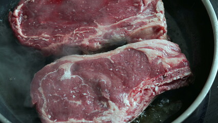 Two raw steaks in a hot pan, starting to cook with salt sprinkled on top, detailed close-up, fresh beef, home kitchen scene, culinary preparation, cooking process, delicious meal beginning