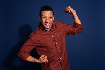 Wall Mural - Photo of lucky cool guy dressed brown shirt rising fists emtpy space isolated blue color background