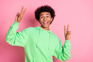 Poster - Portrait of nice young man show v-sign empty space wear green hoodie isolared on pink color background