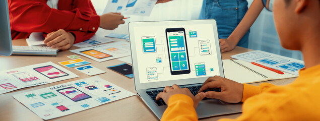 Panorama banner of startup UX developer or company employee design user interface or UI prototype for mobile application or website software with software display on laptop monitor in office. Synergic