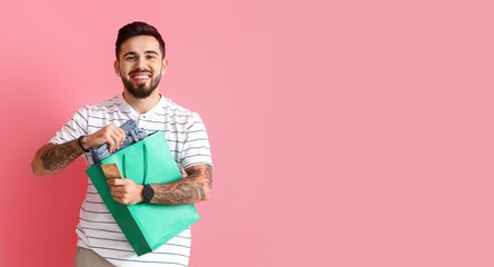 Canvas Print - Handsome man with credit card, shopping bag and new clothes on pink background with space for text