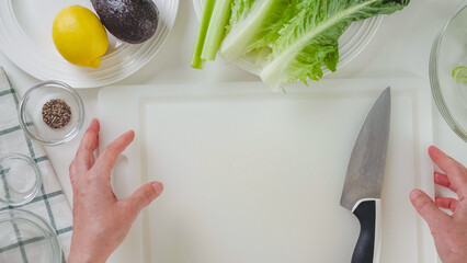 Celery and lettuce salad with avocado, and lemon and olive oil dressing recipe. Ingredients close-up on white background, woman hands