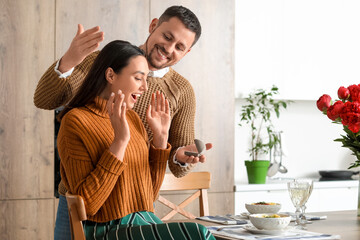 Wall Mural - Young man proposing to his happy girlfriend in kitchen