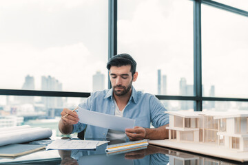 Wall Mural - Skilled caucasian architect engineer holding blueprint on desk in modern office. Smart interior designer compared between blueprint and house model. Project, blueprint, construction, project. Tracery.