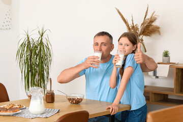 Wall Mural - Little girl with her father drinking milk and showing thumb-up gesture in living room