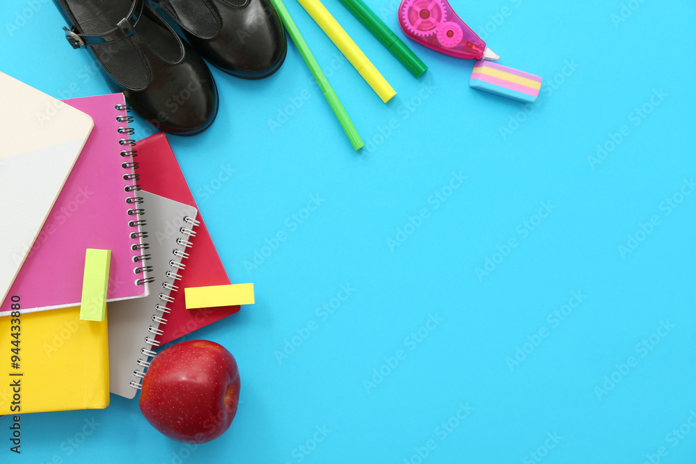 Stylish shoes with red apple and different stationery on blue background