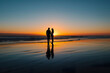 © Mnur - A couple standing on the beach at sunset, with the sun shining on them, generative ai image.