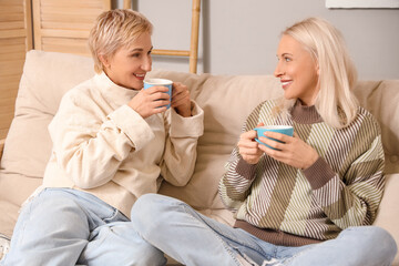 Wall Mural - Mature women with cups of tea sitting on sofa at home