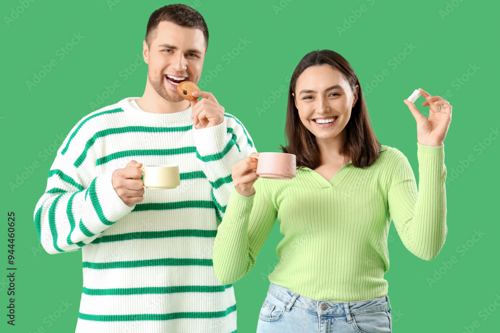Young couple with cookie and sugar drinking tea on green background