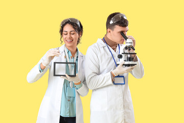 Wall Mural - Young chemists with test tubes and microscope on yellow background